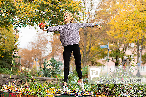 Junge Frau mit blondem Haar steht mit Kürbis in einem städtischen Garten