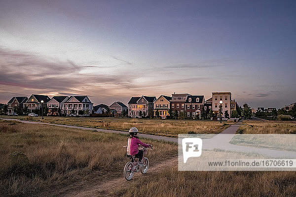 junges Mädchen radelt auf einem unbefestigten Parkweg am Rande eines Wohnviertels