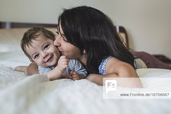 Loving mother kissing sweet smiling baby while lying lying on bed