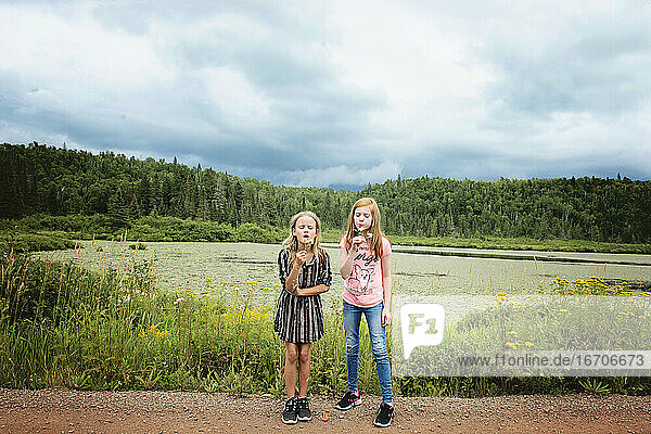 Two Young Girls by Pond Blowing Dandelions
