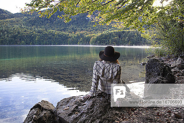Eine Frau sitzt und entspannt unter einem Baum an einem Alpensee