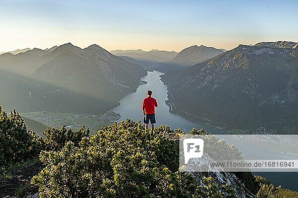 Bergsteiger  junger Mann blickt über Berglandschaft  Latschenkiefern am Gipfel des Bärenkopf  Ausblick auf den Achensee bei Sonnenuntergang  links Seekarspitze und Seebergspitze  Karwendel  Tirol  Österreich  Europa