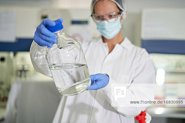 Weibliche Wissenschaftlerin mit Gesichtsmaske und Handschuh untersucht eine Flüssigkeit im Labor