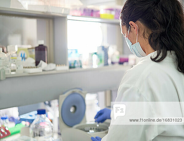 Wissenschaftlerin mit Gesichtsmaske an Zentrifuge im Labor