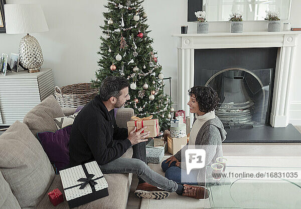 Ehemann gibt Weihnachtsgeschenk an Frau durch Baum im Wohnzimmer