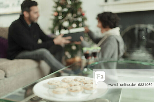 Ehefrau öffnet Weihnachtsgeschenk von Ehemann hinter Tablett mit Mince Pies
