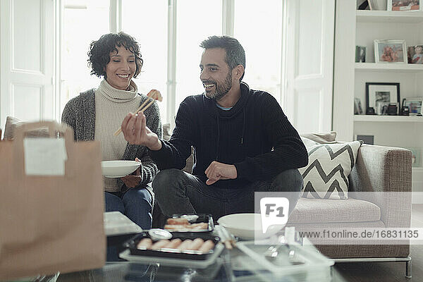 Glückliches Paar isst Essen zum Mitnehmen mit Stäbchen im Wohnzimmer