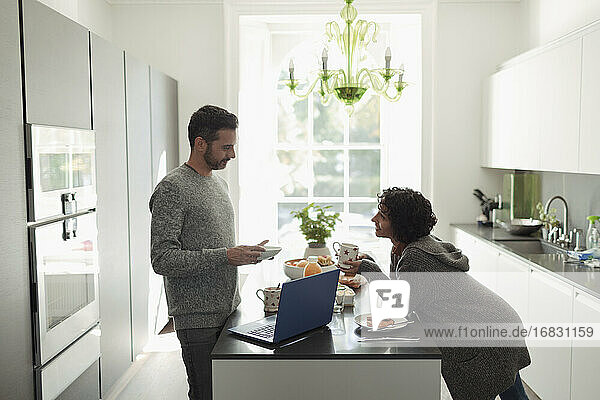 Paar im Gespräch und genießen das Frühstück am Laptop in der Küche am Morgen