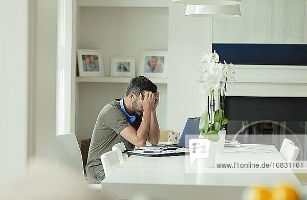 Tired man with head in hands working from home at laptop