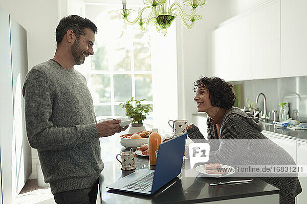 Glückliches Paar genießt das Frühstück und arbeitet am Laptop in der Küche