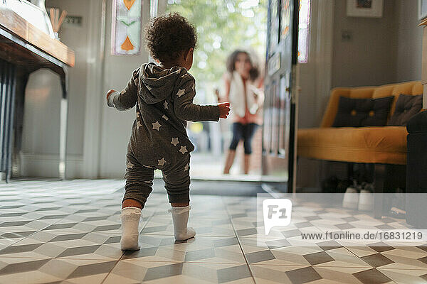 Nettes Baby-Mädchen in Stern-Pyjamas zu Fuß zur Mutter an der offenen Tür