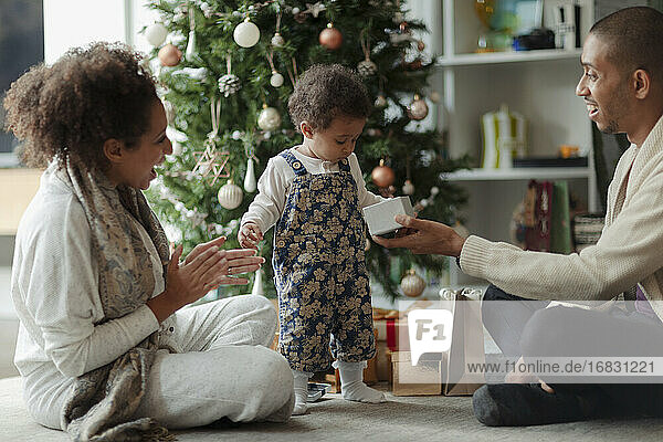 Glückliche Eltern und Baby Tochter Öffnung Weihnachtsgeschenk durch Baum