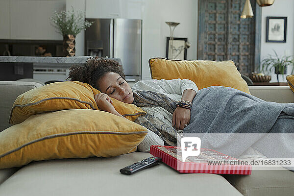 Müde Frau schläft auf dem Sofa neben einer Schachtel Pralinen