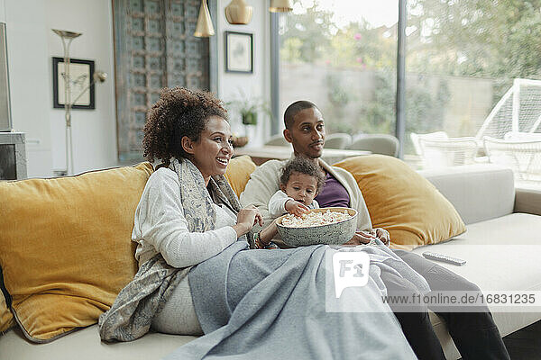 Parents with baby daughter watching movie with popcorn on sofa