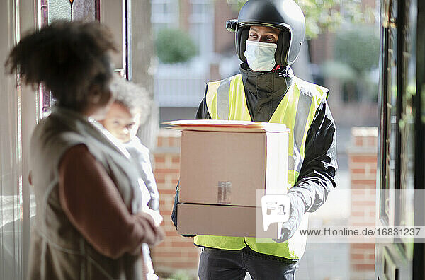 Frau empfängt Pakete vom Zusteller mit Gesichtsmaske an der Haustür