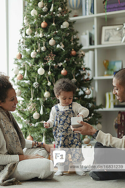 Paar hilft Baby Tochter öffnen Weihnachtsgeschenk im Wohnzimmer