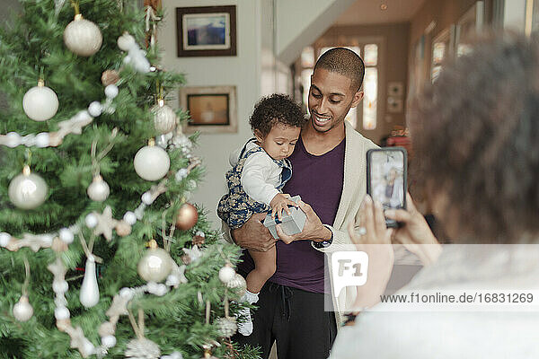 Frau fotografiert Mann und kleine Tochter am Weihnachtsbaum