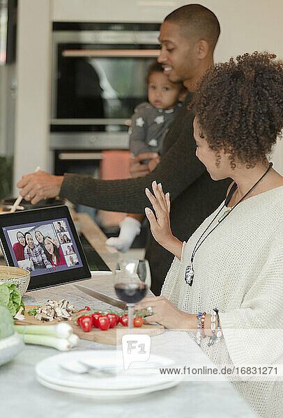 Family video chatting at digital tablet and cooking in kitchen