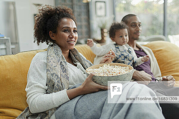 Glückliche Familie beobachten Film und essen Popcorn auf Sofa im Wohnzimmer