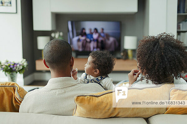 Eltern und Baby Tochter vor dem Fernseher auf dem Sofa im Wohnzimmer