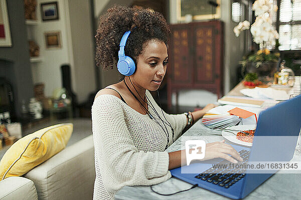 Frau mit Kopfhörer arbeiten am Laptop auf Esstisch