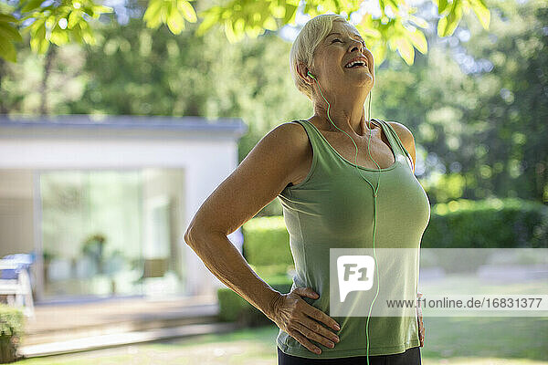 Carefree senior woman with headphones exercising in summer garden
