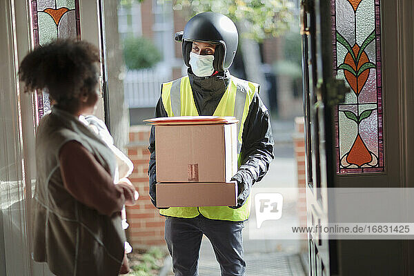 Frau empfängt Pakete vom Zusteller mit Gesichtsmaske an der Haustür