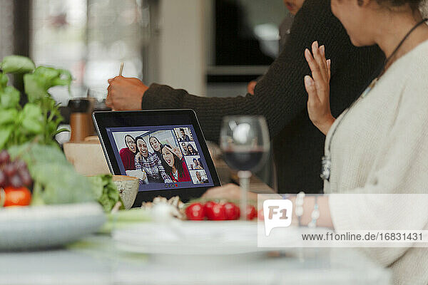Familie beim Videochat auf dem digitalen Tablet-Bildschirm und bei der Zubereitung des Abendessens