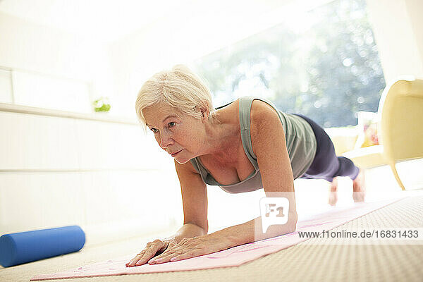 Fokussierte ältere Frau übt Planke Übung auf Yoga-Matte zu Hause