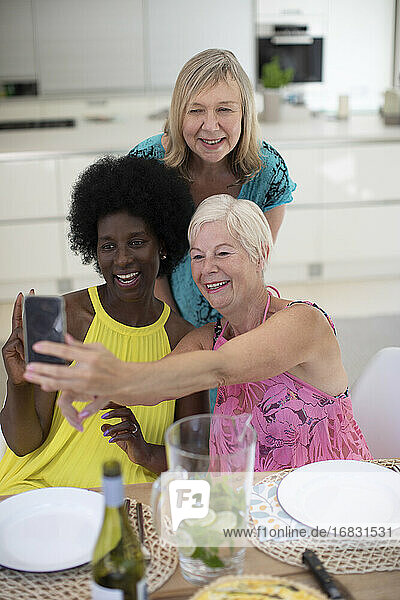 Glückliche ältere Frauen Freunde in Kleidern nehmen selfie am Esstisch