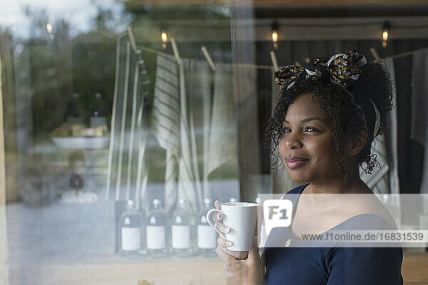 Nachdenkliche Ladenbesitzerin trinkt Kaffee am Schaufenster