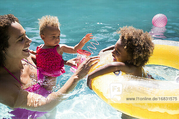 Mutter und Töchter spielen im sonnigen Sommer Schwimmbad