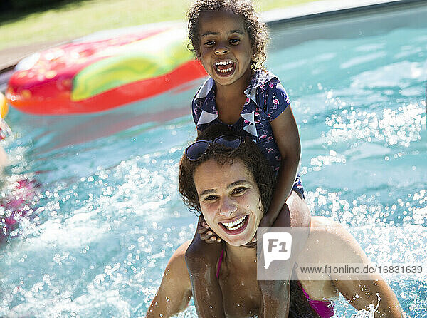 Portrait happy mother carrying daughter on shoulders in swimming pool