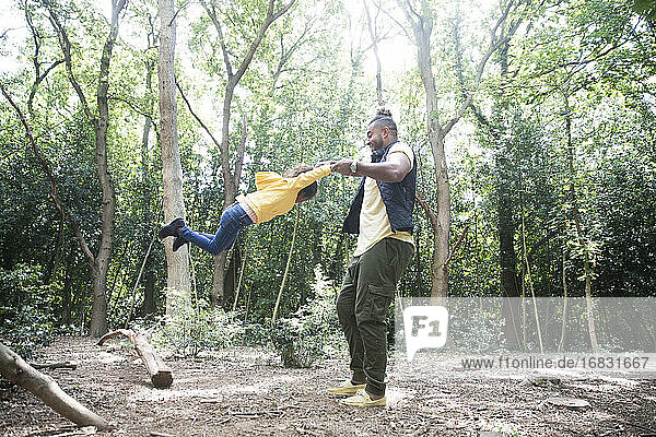 Playful father swinging daughter below trees in sunny woods
