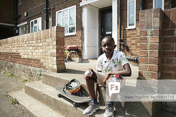 Portrait confident boy with skateboard on sunny front stoop