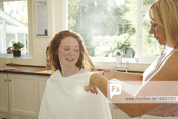 Mutter schneiden Haare für preteen Tochter in sonnigen Küche