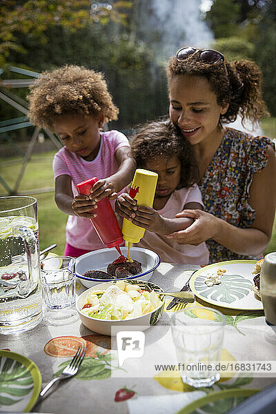 Mother and daughters enjoying summer backyard barbecue at table