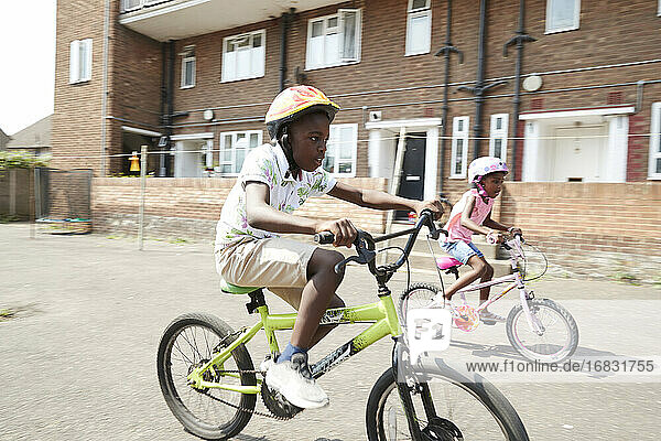 Brother and sister riding bikes in sunny neighborhood