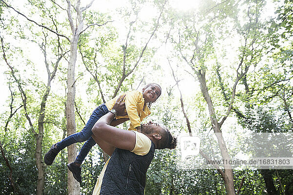 Playful sorglos Vater Heben Tochter unter Bäumen in sonnigen Park