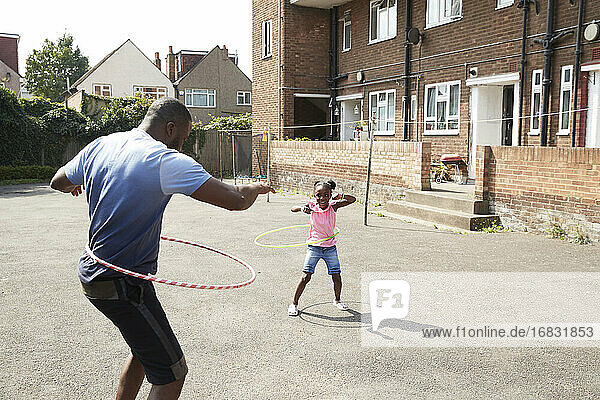 Vater und Tochter spielen mit Plastikreifen in sonniger Nachbarschaft