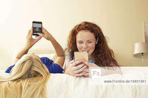 Preteen girl friends using smart phones on bed