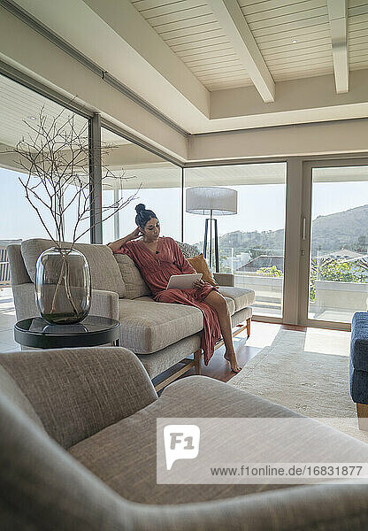 Frau entspannt mit digitalem Tablet auf Sofa in Luxus-Wohnzimmer
