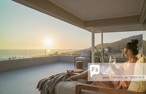 Woman enjoying white wine and sunset ocean view on luxury balcony