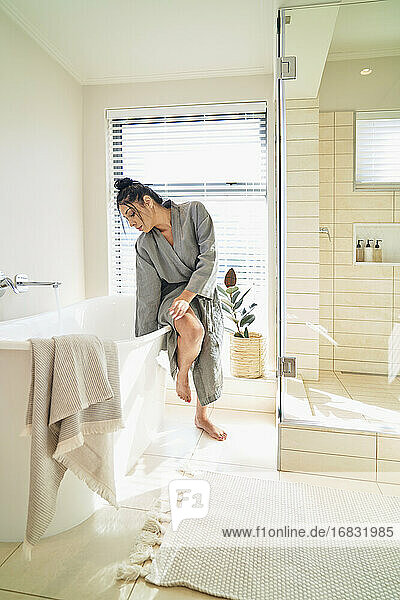 Frau im Bademantel bereitet Einweichwanne für Bad in sonnigen Badezimmer