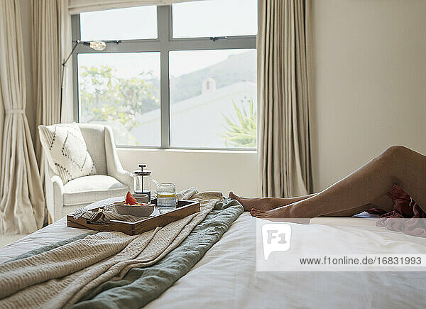 Barfuß Frau entspannt auf Bett mit Frühstückstablett im Schlafzimmer