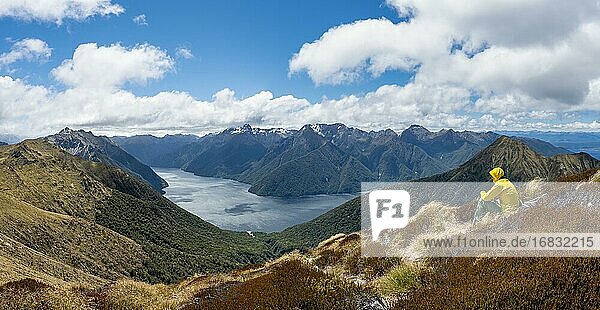 Mountaineer  hiker sitting in the grass  view of the South Fiord of Lake Te Anau  Murchison Mountains and Southern Alps in the background  on the Kepler Track hiking trail  Fiordland National Park  Southland  New Zealand  Oceania