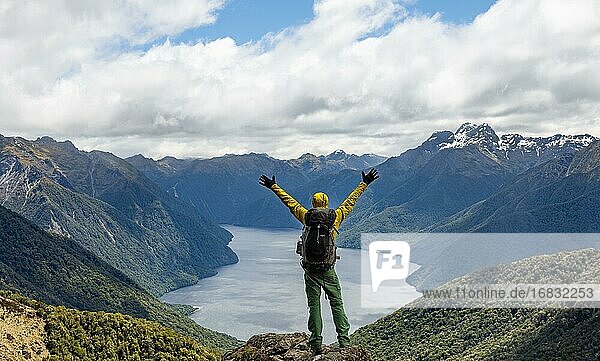 Bergsteiger  Wanderer blickt in die Ferne  streckt Arme in die Luft  Ausblick auf den South Fiord des Lake Te Anau  hinten Murchison Mountains und Südalpen  am Wanderweg Kepler Track  Fiordland National Park  Southland  Neuseeland  Ozeanien