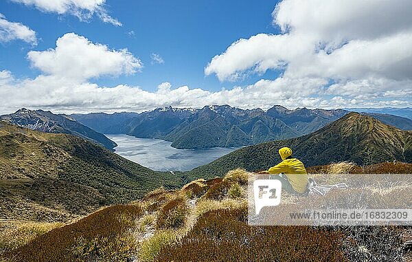 Mountaineer  hiker sitting in the grass  view of the South Fiord of Lake Te Anau  in the back Murchison Mountains and Southern Alps  on the hiking trail Kepler Track  Fiordland National Park  Southland  New Zealand  Oceania