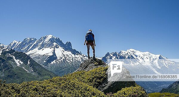 Hiker standing on rocks  mountain panorama from Aiguillette des Posettes  left summit of Aiguille Verte (right) Aiguille du Midi and Mont Blanc  Chamonix  Haute-Savoie  France  Europe