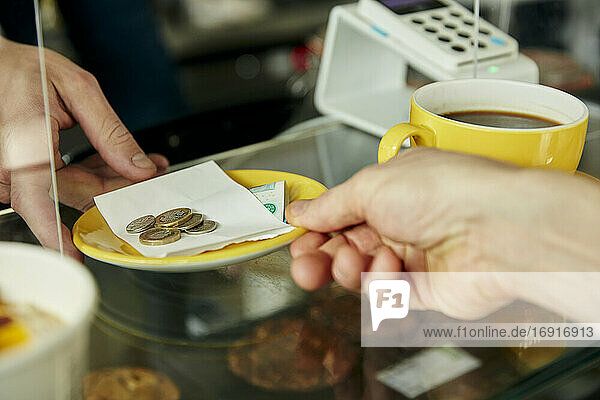 Nahaufnahme von Händen tauschen Platte mit Geld für die Zahlung in Café